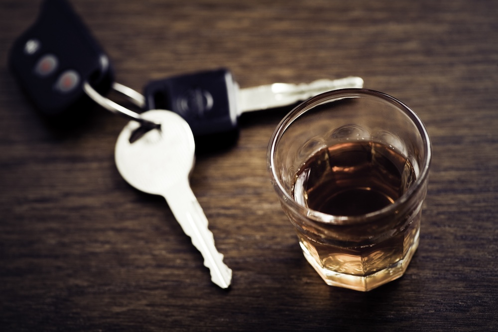 A shot glass full of dark colored alcohol on top of a bar table along with a set of car keys. Drinking and driving surges at the holidays in Houston.