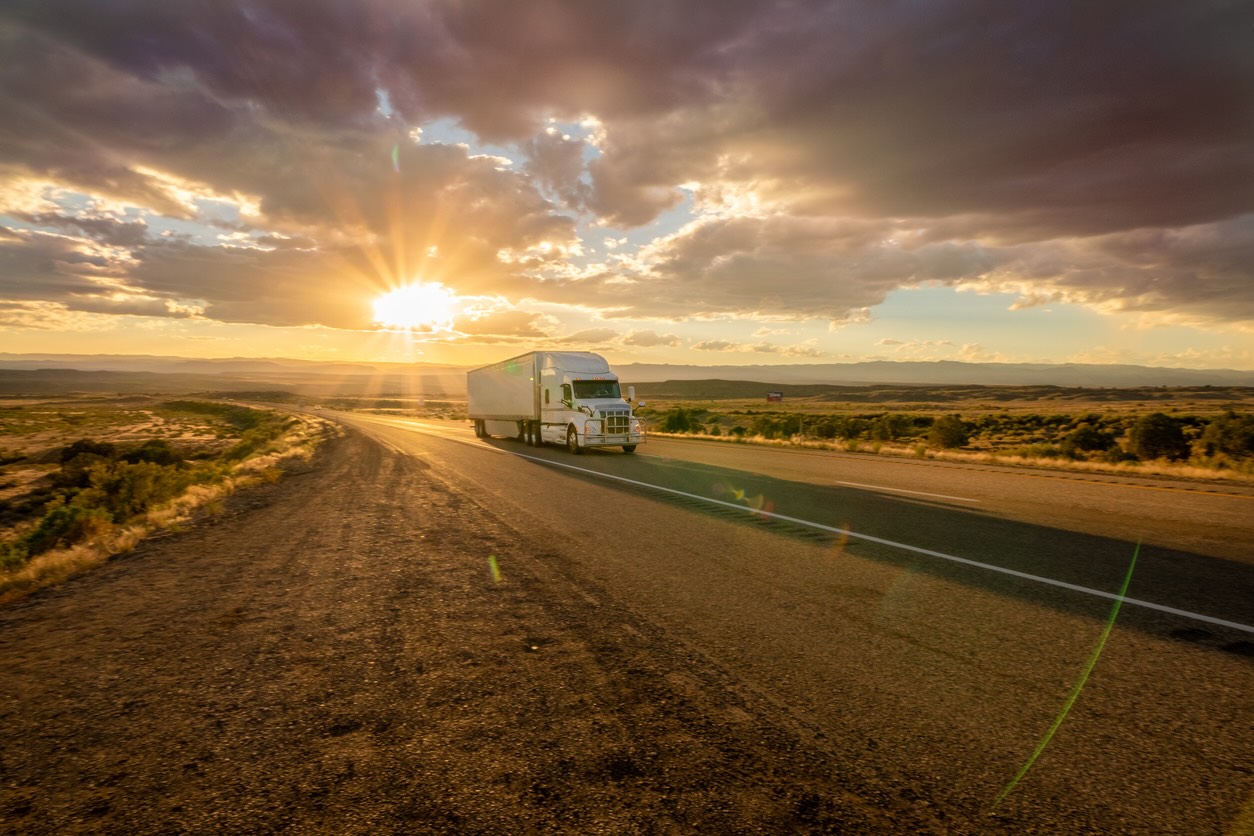 A massive oilfield truck driving on a Texas road at sunset.