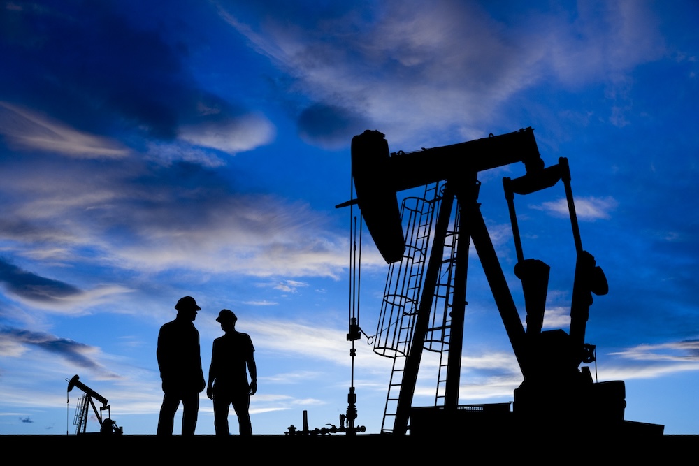 Two oilfield workers near dangerous heavy equipment at dusk.