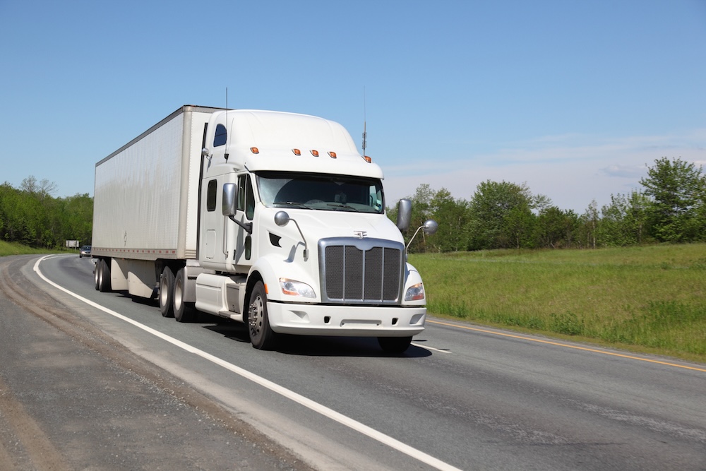 An all-white 18-wheeler drives a two-lane highway.